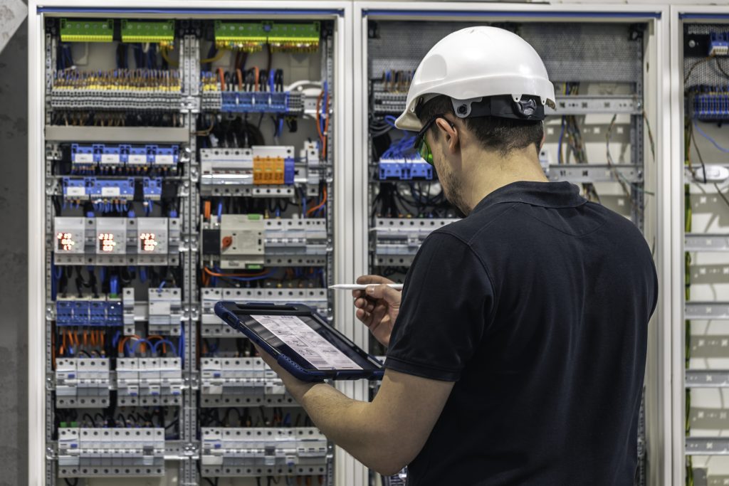 man electrical working switchboard with fuses uses tablet